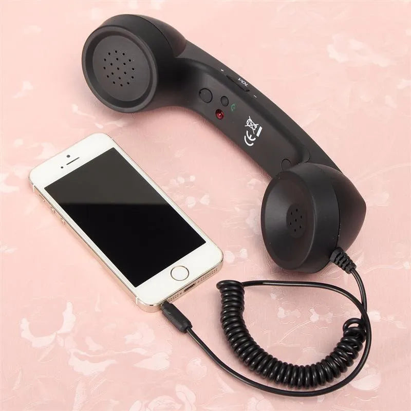 Black retro-style telephone handset with coiled cord plugged into a white smartphone on a soft pink background.