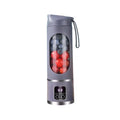 Grey portable blender with a digital display, transparent central window, and carry strap, filled with fruit.