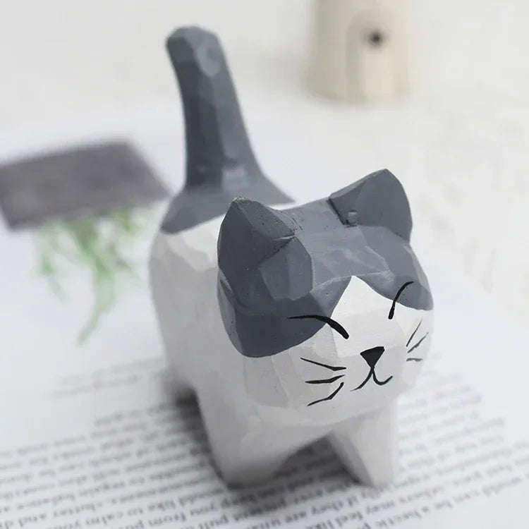 Small, hand-carved wooden cat figurine with a grey and white painted finish and a cute, minimalist smiling face.
