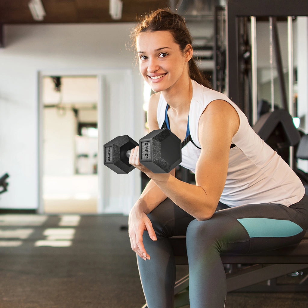 Woman smiling while lifting a black 12.5kg rubber hex dumbbell in a gym.