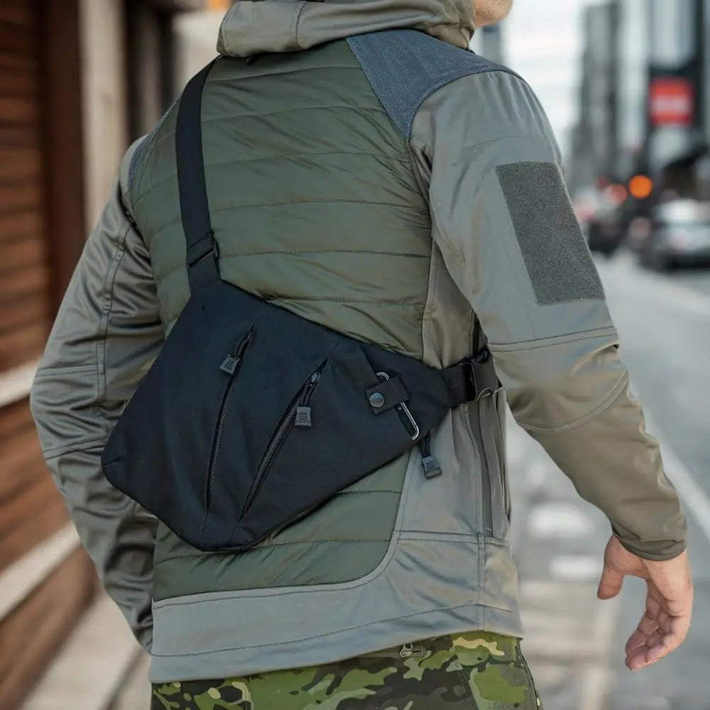 A person wearing a sleek, black triangular anti-theft crossbody sling bag with secure zip compartments and a strap.