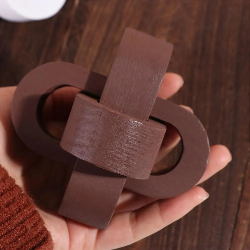 Hand holding a small, brown wooden puzzle shaped like interlocking loops with a smooth, matte finish.
