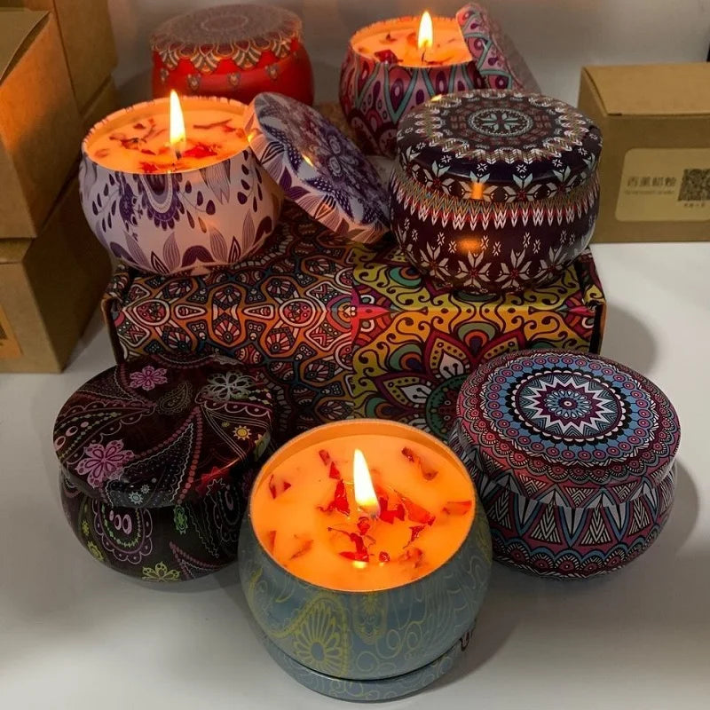 Set of decorative scented candles in colourful, patterned metal tins with lids, some lit with petal-topped wax.