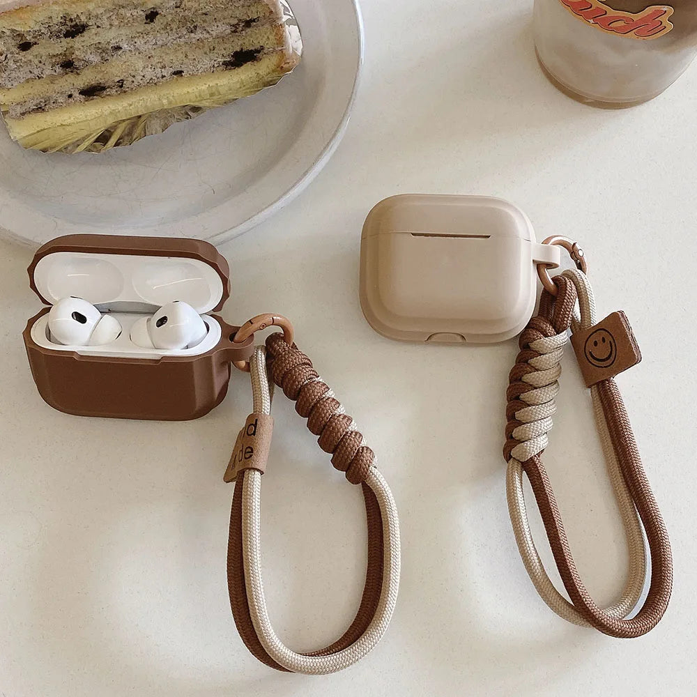 Matte silicone AirPods Pro cases in mocha and beige, featuring braided wrist straps with smiley face charms.