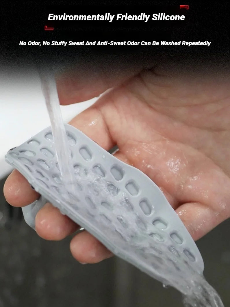 A hand washing a grey, flexible silicone textured pad under running water.