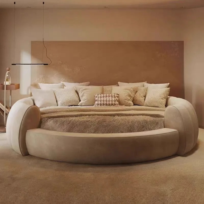 Minimalist beige circular bedside table with a smooth, curved design next to a large round bed in a neutral room.