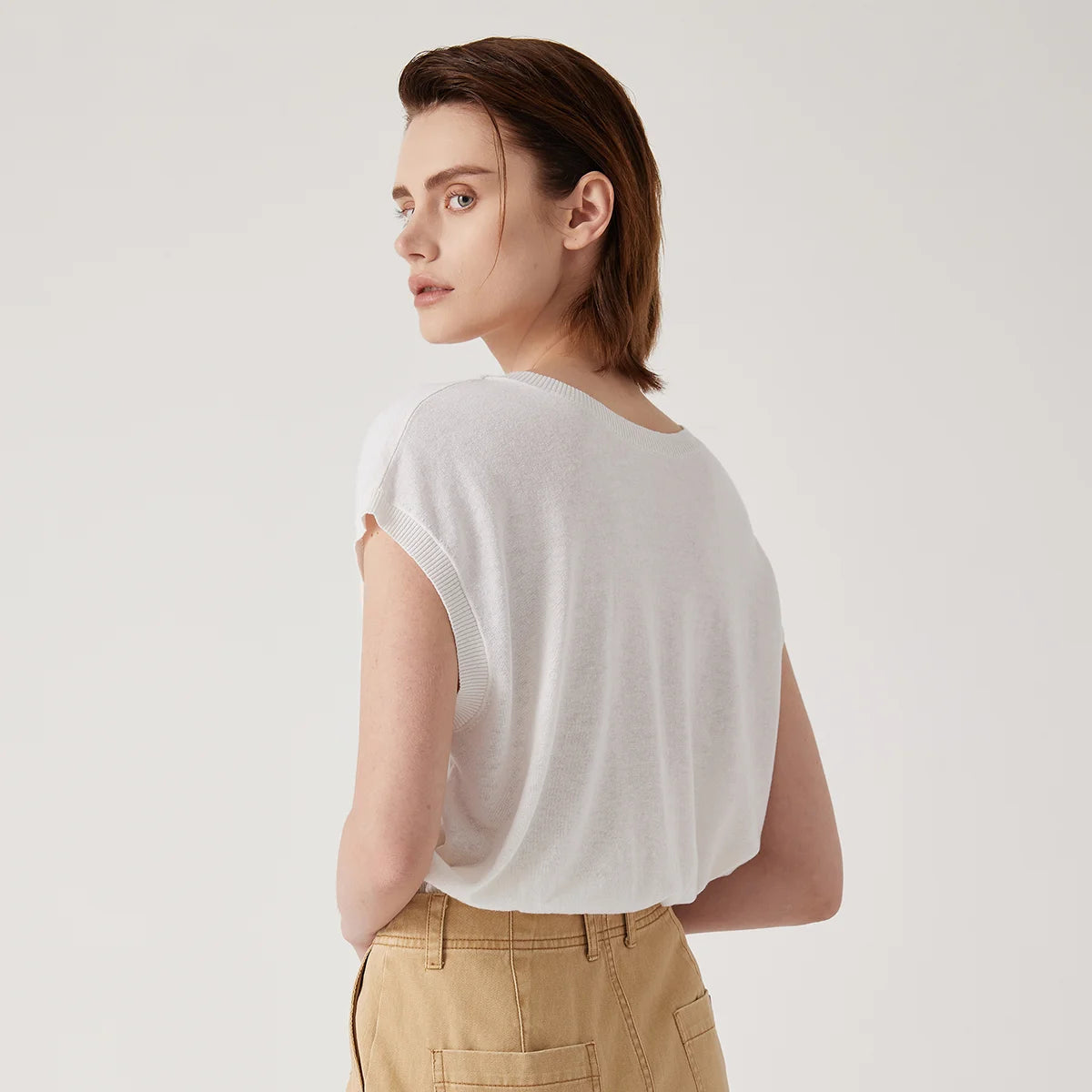 Woman wearing a white, lightweight, short-sleeved round-neck knit top paired with beige utility-style trousers.