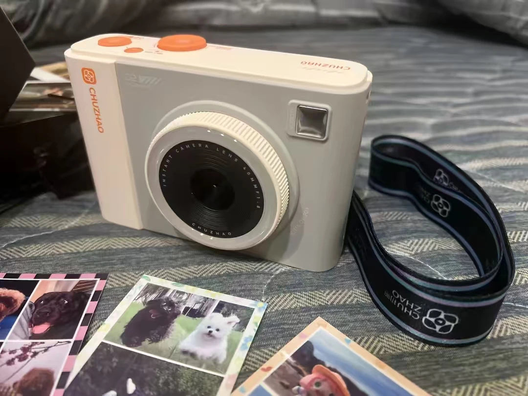 Off-white plastic instant camera with orange buttons, a 40mm lens, and a black branded camera strap.