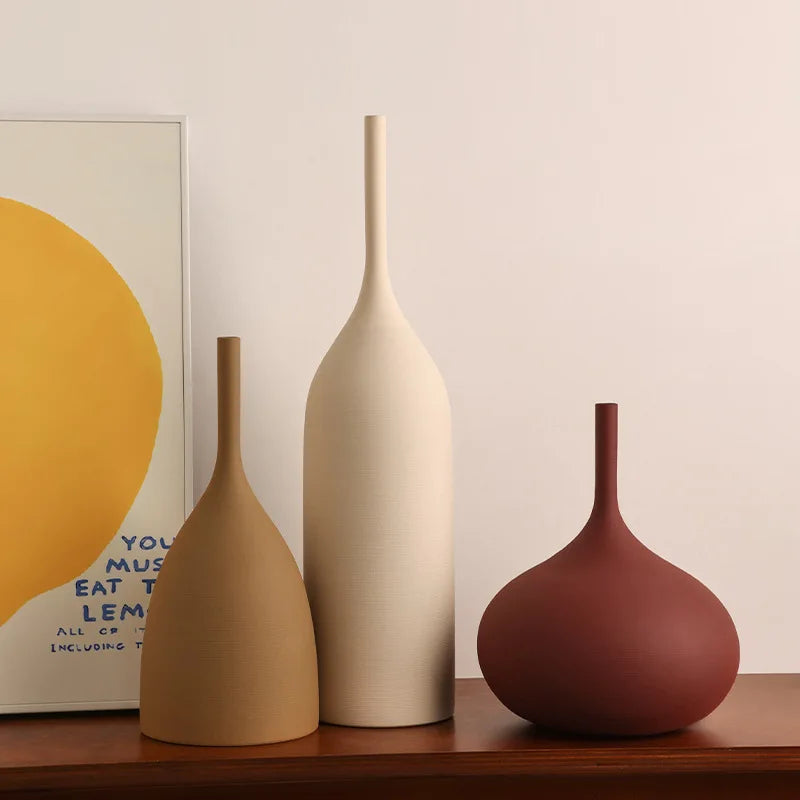 Three minimalist handmade ceramic vases in mustard, cream, and terracotta with slender necks and textured finishes.