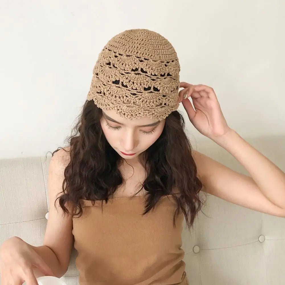 A woman wearing a beige, hollow crochet lace beanie with a decorative scalloped edge design.