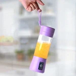 Portable purple personal blender with a carrying strap, filled with yellow fruit juice, held by a hand.