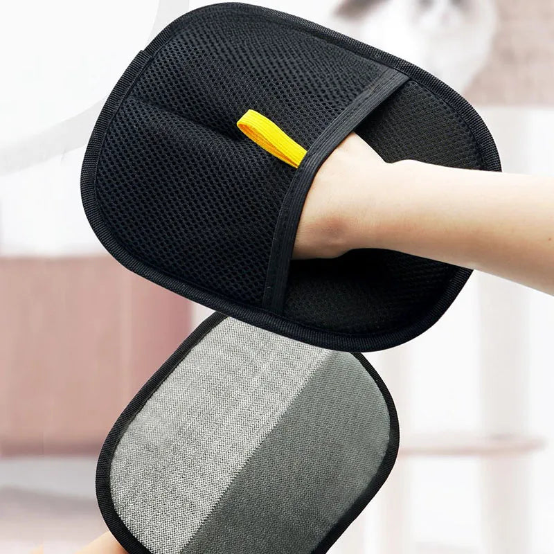 A hand wearing a black mesh cleaning mitt with a yellow loop, held above a grey and dark grey scrub pad.