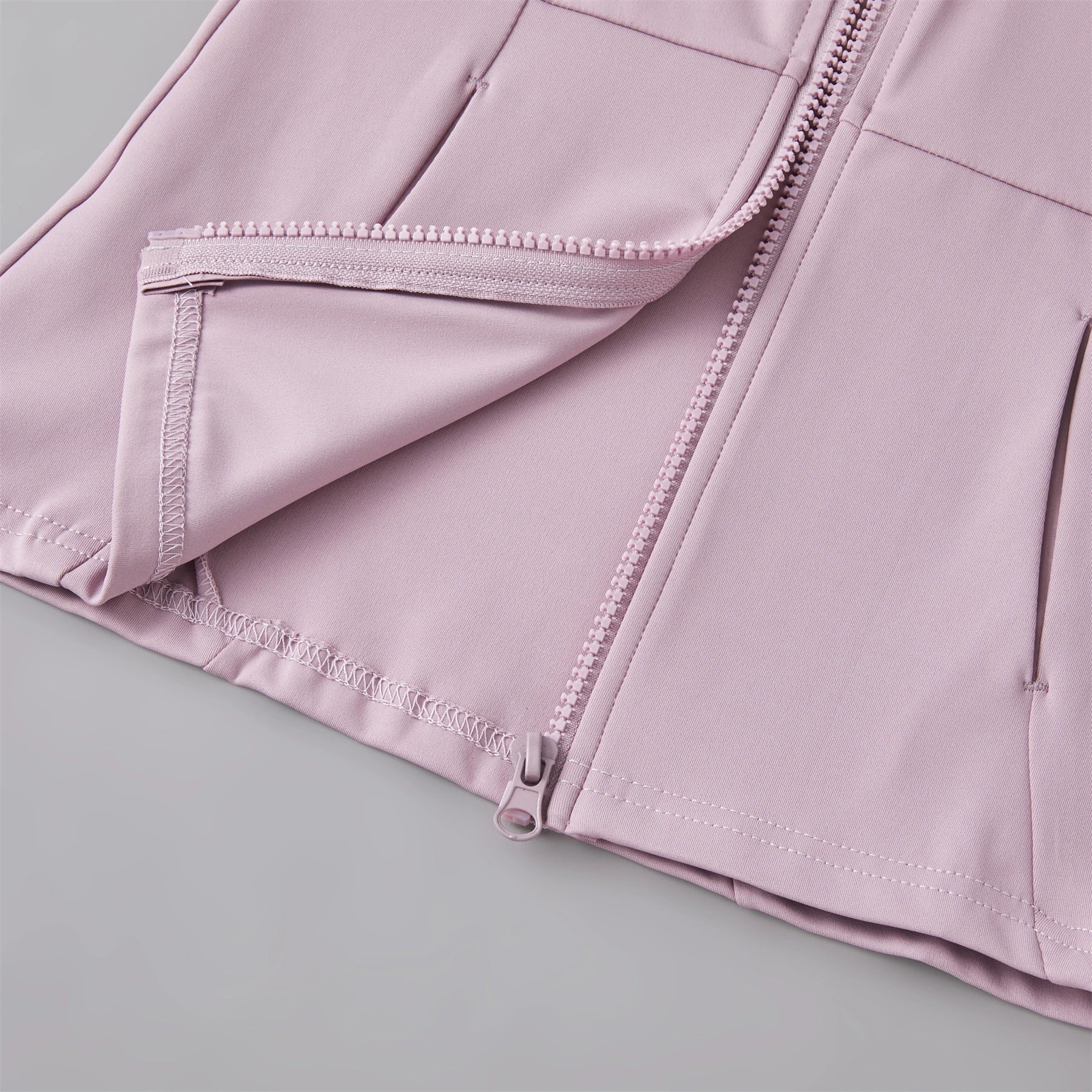 Close-up of a dusty pink lightweight zipped jacket featuring clean seams and secure zip pockets.