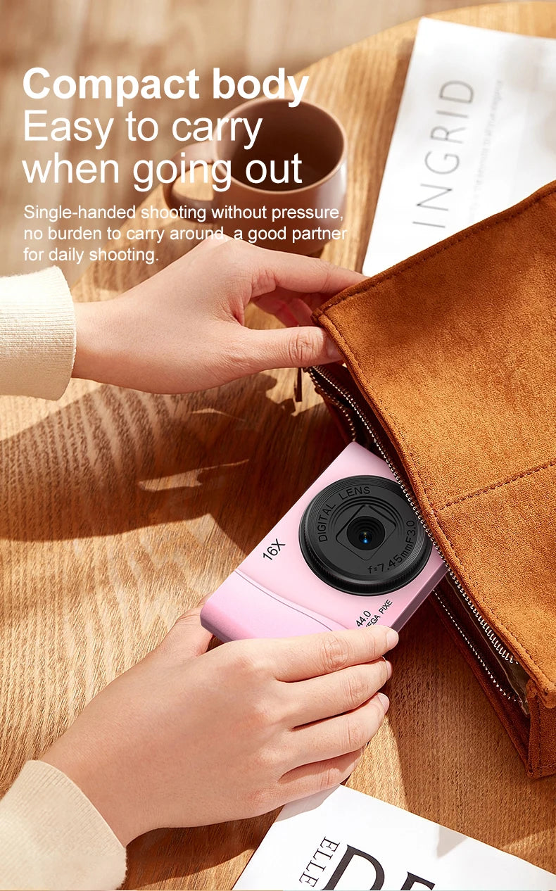 A small, smooth light pink plastic digital camera with a 16x zoom lens being placed into a brown suede bag.