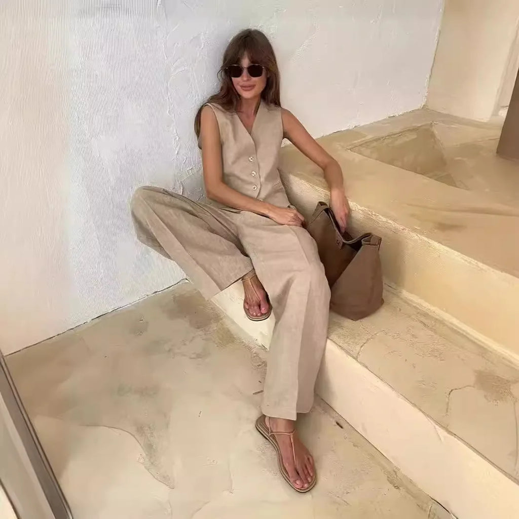 Woman wearing a beige linen waistcoat and matching wide-leg trousers, styled with sandals and a brown tote bag.