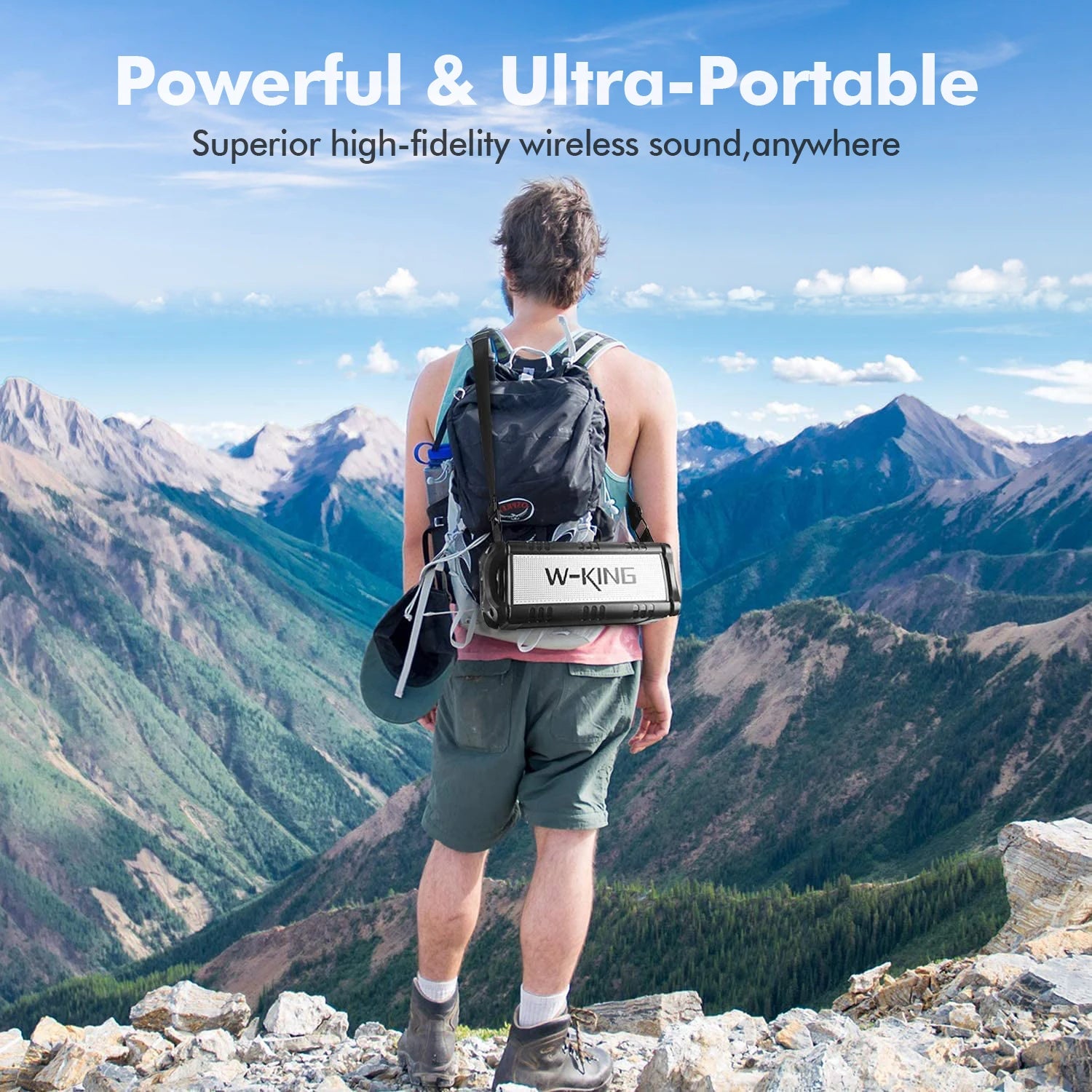 A hiker stands on a mountain ridge wearing a black portable 90W waterproof wireless Bluetooth speaker with a shoulder strap.