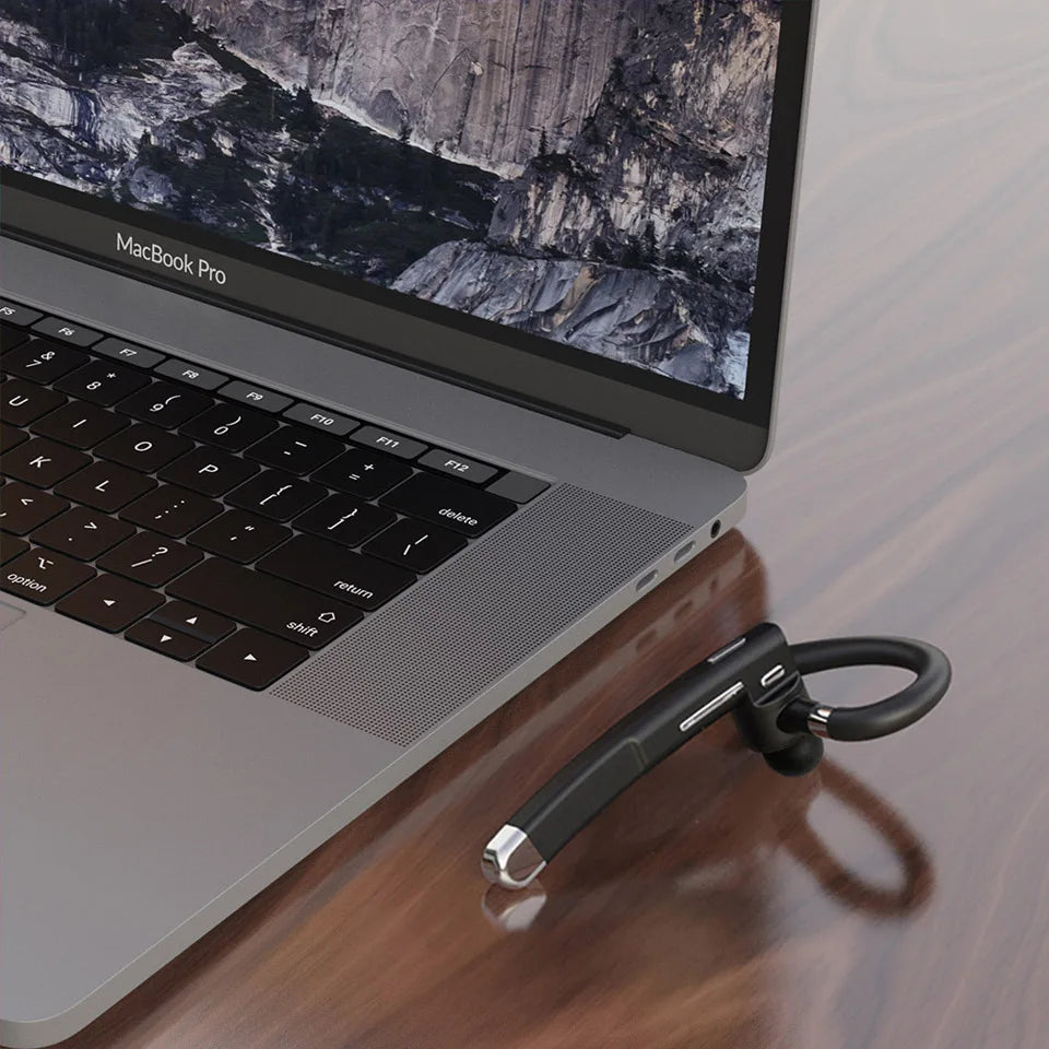 Sleek black wireless earpiece with a hook design, microphone, and silver accents, resting next to a laptop.