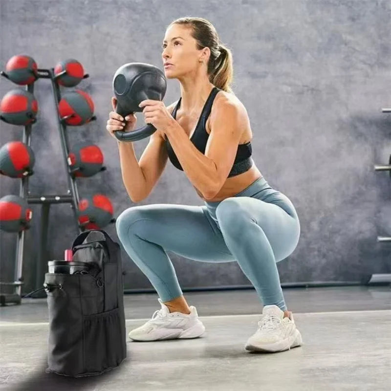 Woman in blue leggings squatting with a black kettlebell, with a black gym bottle bag in the foreground.