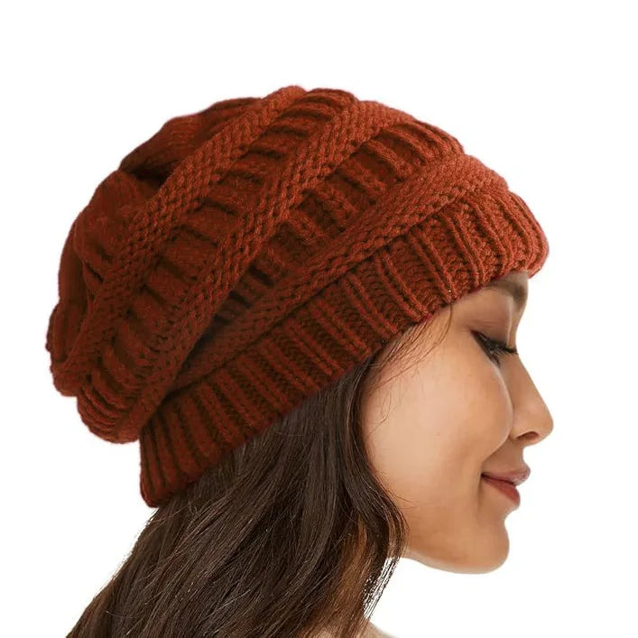 Side profile of a woman wearing a rust-coloured, cable-knit winter beanie with a ribbed cuff.