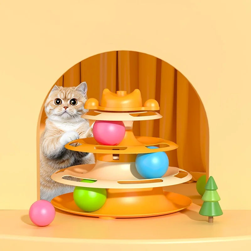 A cat plays with a three-tiered orange interactive toy featuring rolling pink, blue, and green balls on a yellow base.