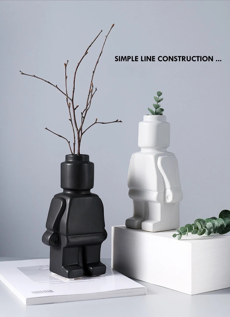Two modern robot-shaped ceramic vases in matte black and white, perfect for minimalist floral displays.