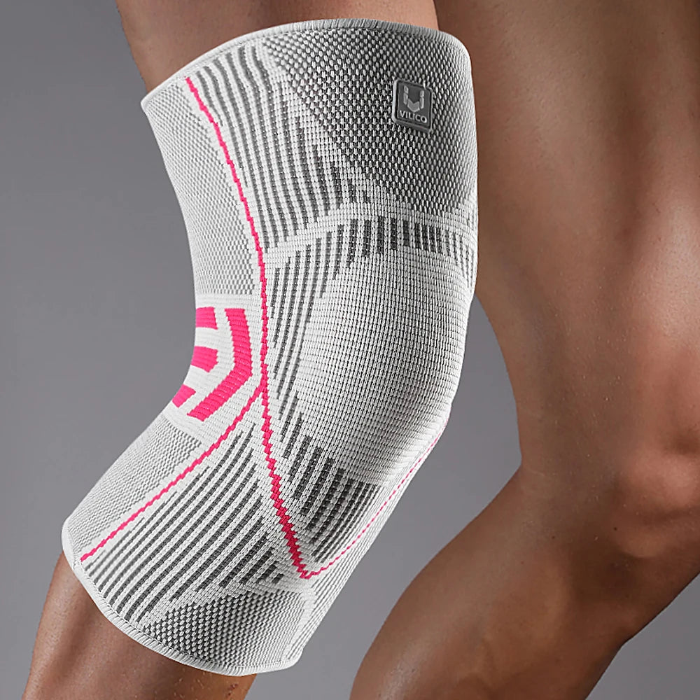 A white and grey compression knee sleeve with pink accents worn on a leg.