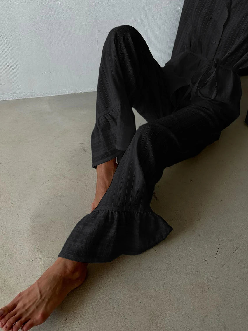 Black textured trousers with a ruffled hem, styled in a relaxed fit with a matching tie-waist shirt.