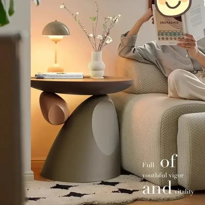 Minimalist sculptural side table in a soft taupe cream finish, featuring an artistic organic base next to a sofa.