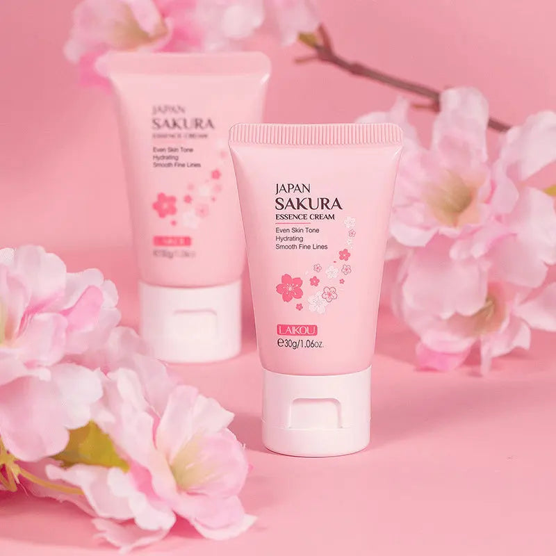 Two pink tubes of hydrating sakura essence cream, featuring floral decorations against a matching pink background.
