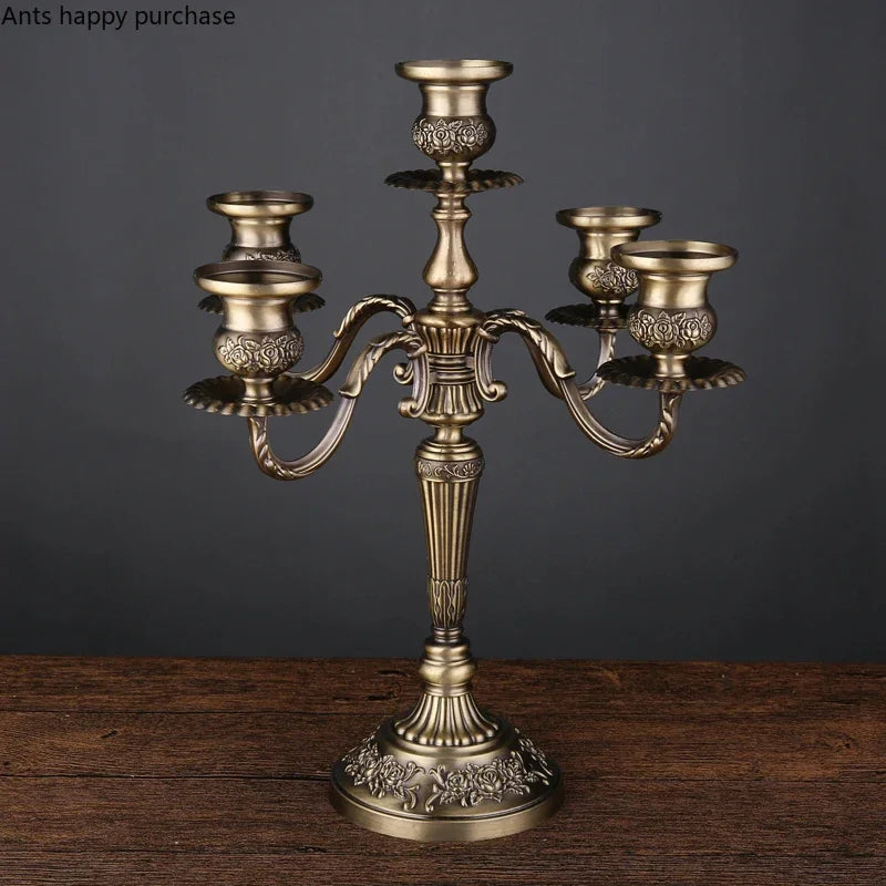 Antique bronze 5-arm candelabra with ornate floral relief on the base and candle cups, standing on a wooden surface.