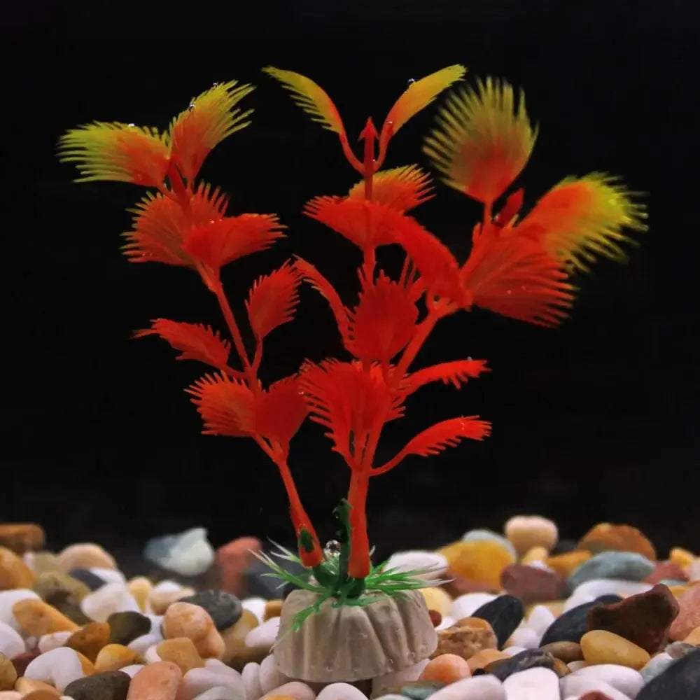 Artificial aquarium plant with orange and yellow feathery leaves on a grey base, set against a black background.