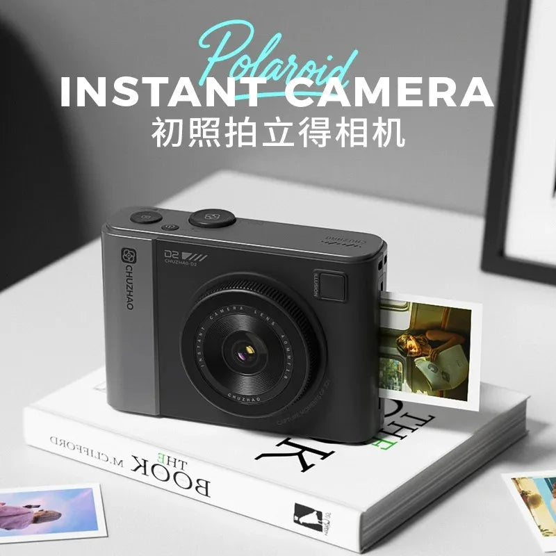 A sleek, matte grey instant camera by Chuzhao, sitting on a book and ejecting a printed photo.