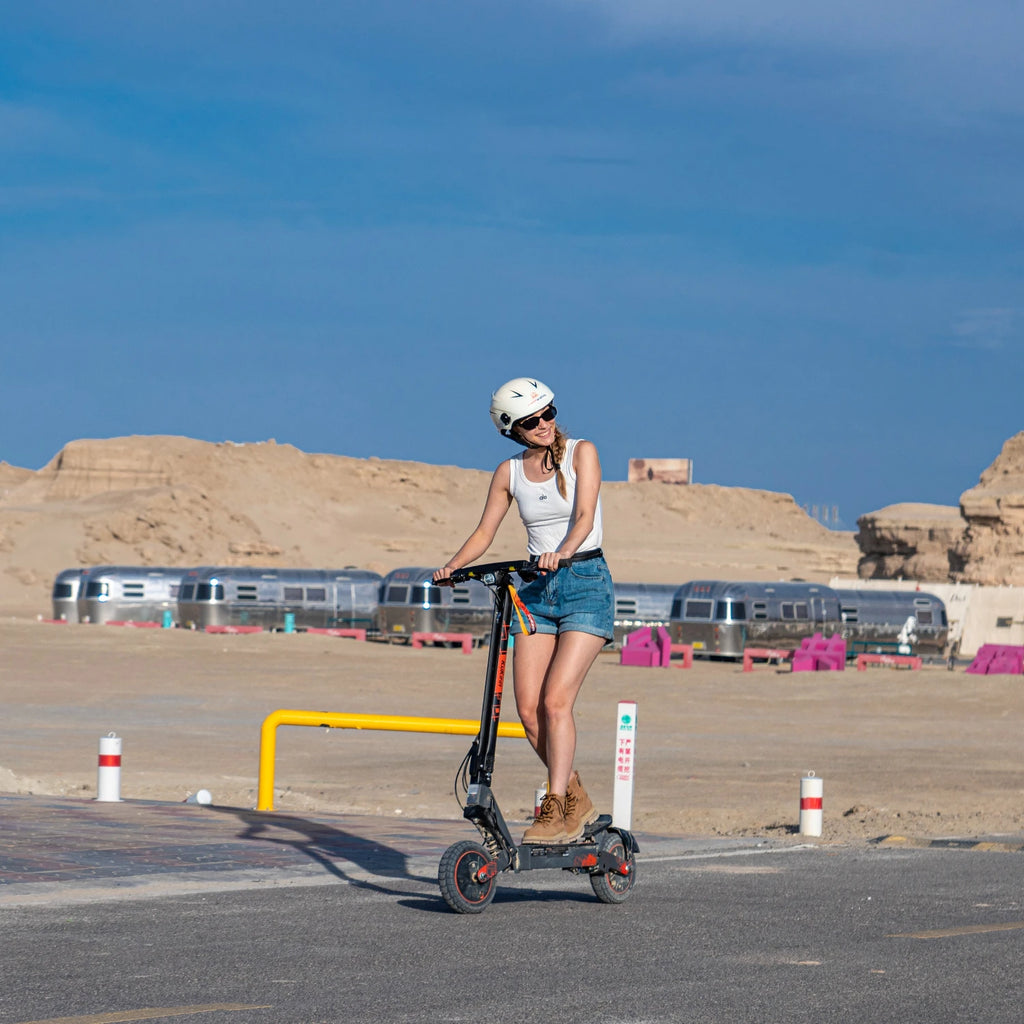 Woman in helmet riding a black KuKirin G2 Ultra electric scooter with 10-inch tires on a paved desert road.