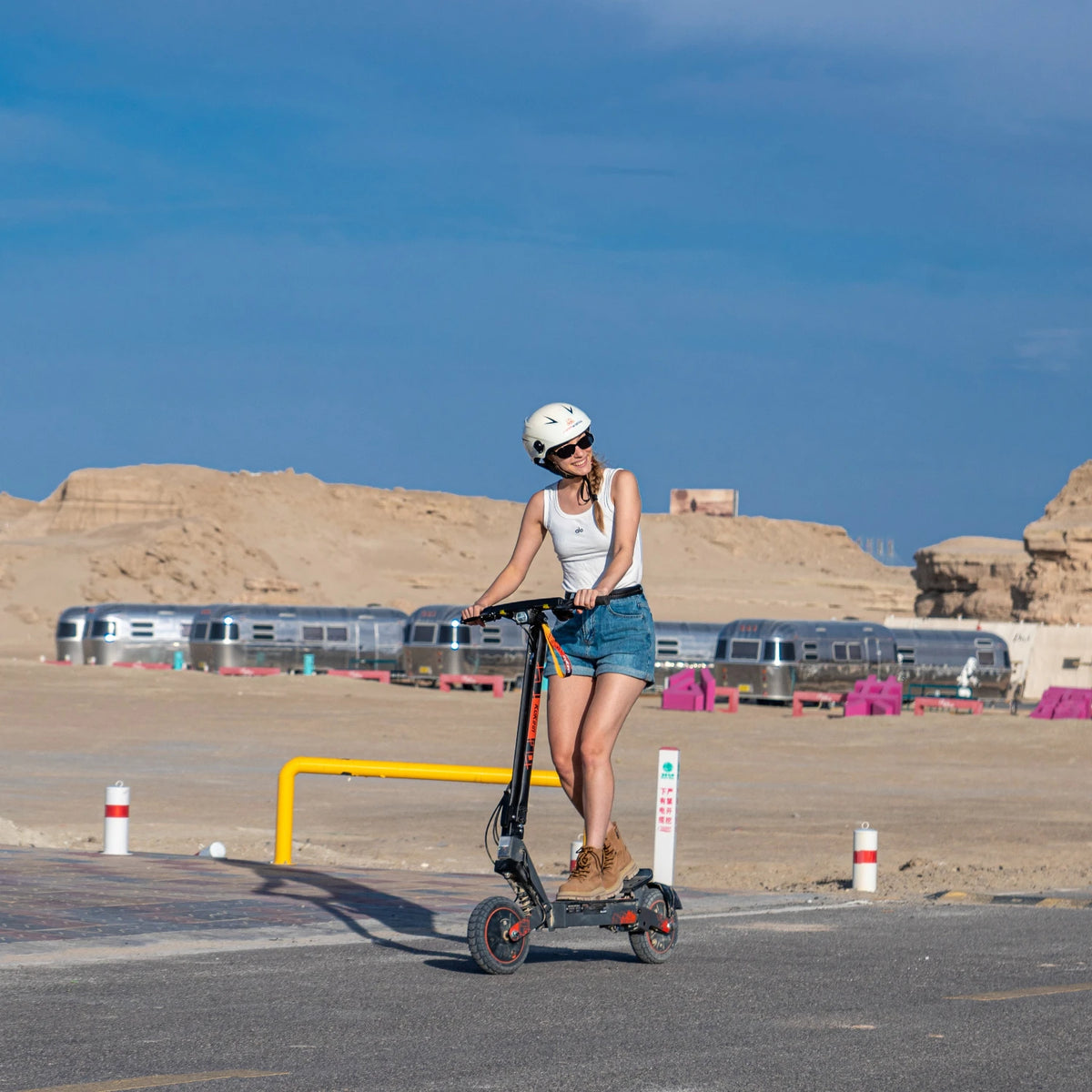 Woman in helmet riding a black KuKirin G2 Ultra electric scooter with 10-inch tires on a paved desert road.