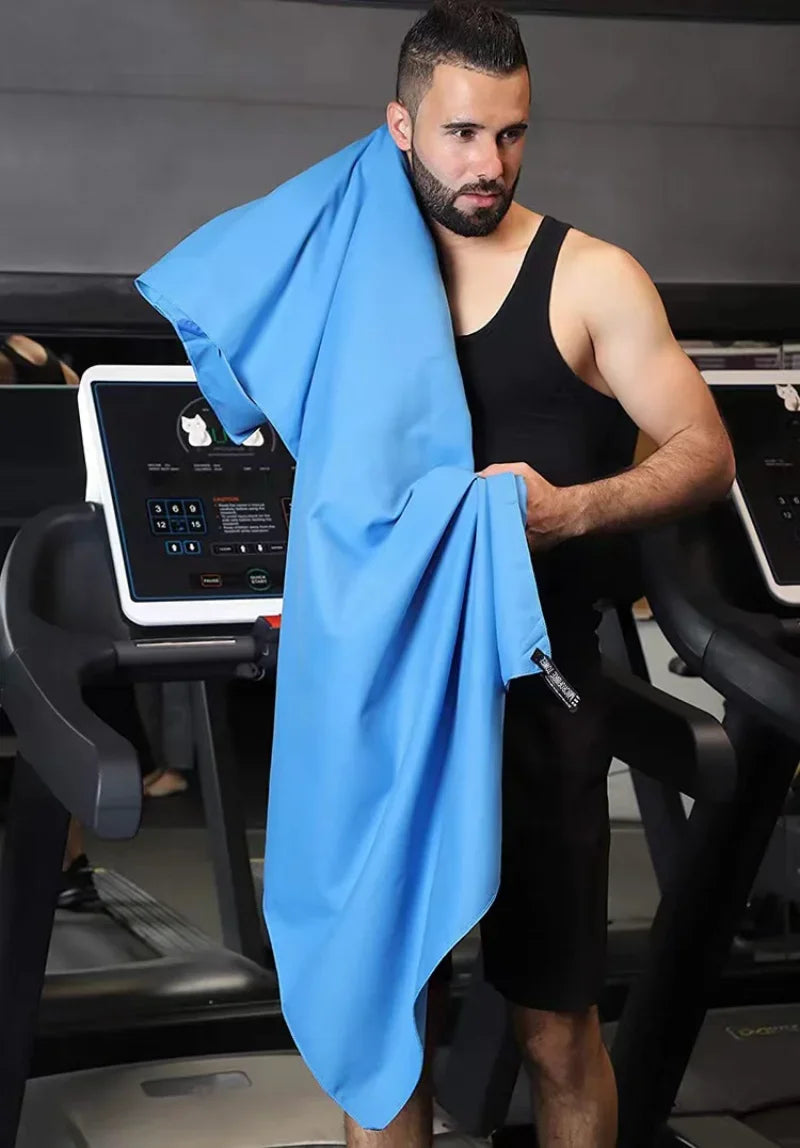 A man in a gym holding a bright blue, smooth-textured microfibre towel over his shoulder.