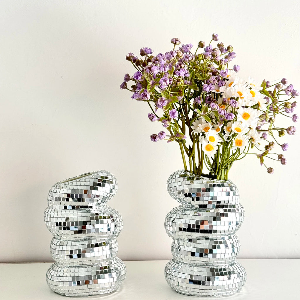 Two silver, disco ball-style mirrored vases with an uneven, stacked design, one holding purple and white flowers.