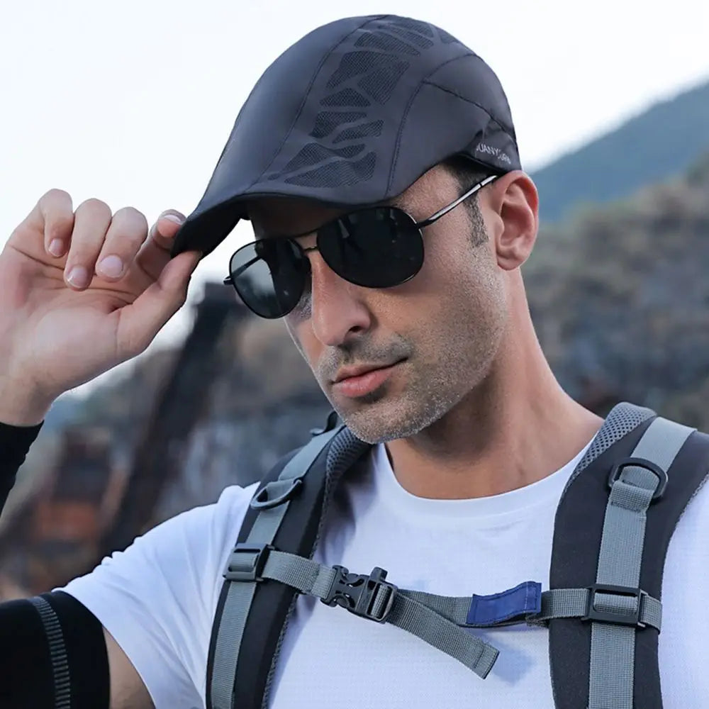 A man wearing a dark grey, lightweight newsboy flat cap with a subtle geometric pattern and a short curved peak.