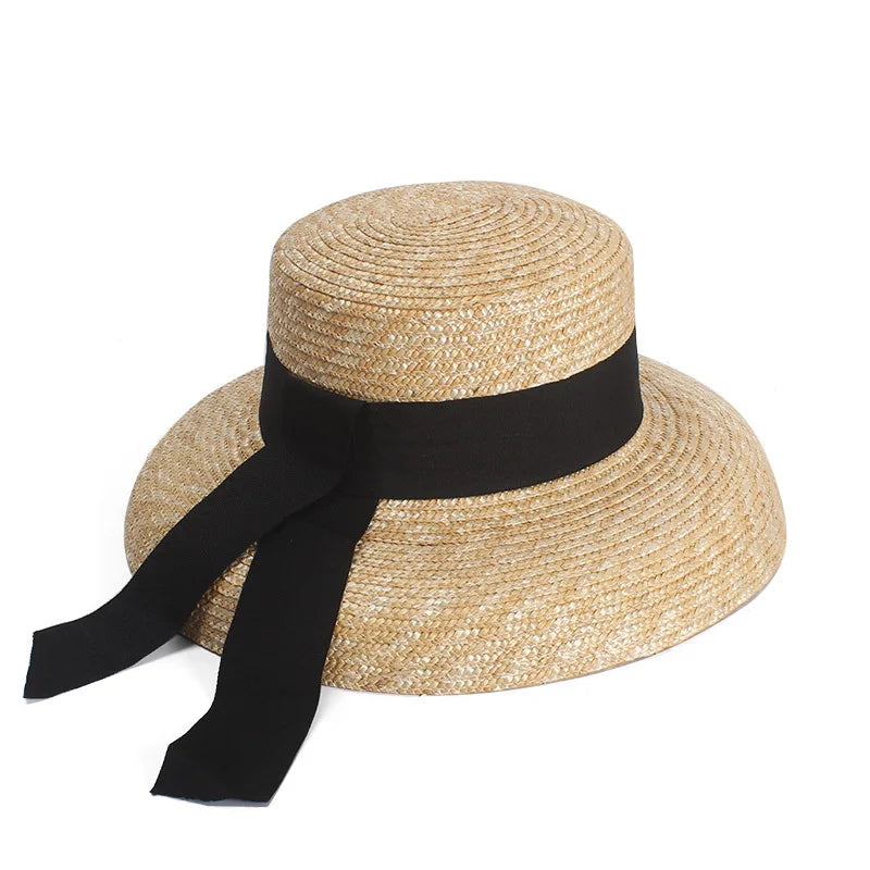 Elegant natural straw sun hat with a wide brim, flat top, and a decorative black ribbon tied at the side.