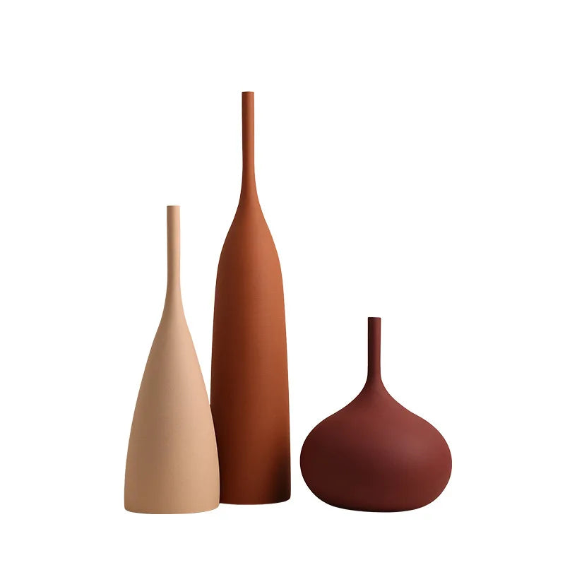 Three minimalist handmade ceramic vases in graduated terracotta, rust, and cream tones with sleek, organic silhouettes.