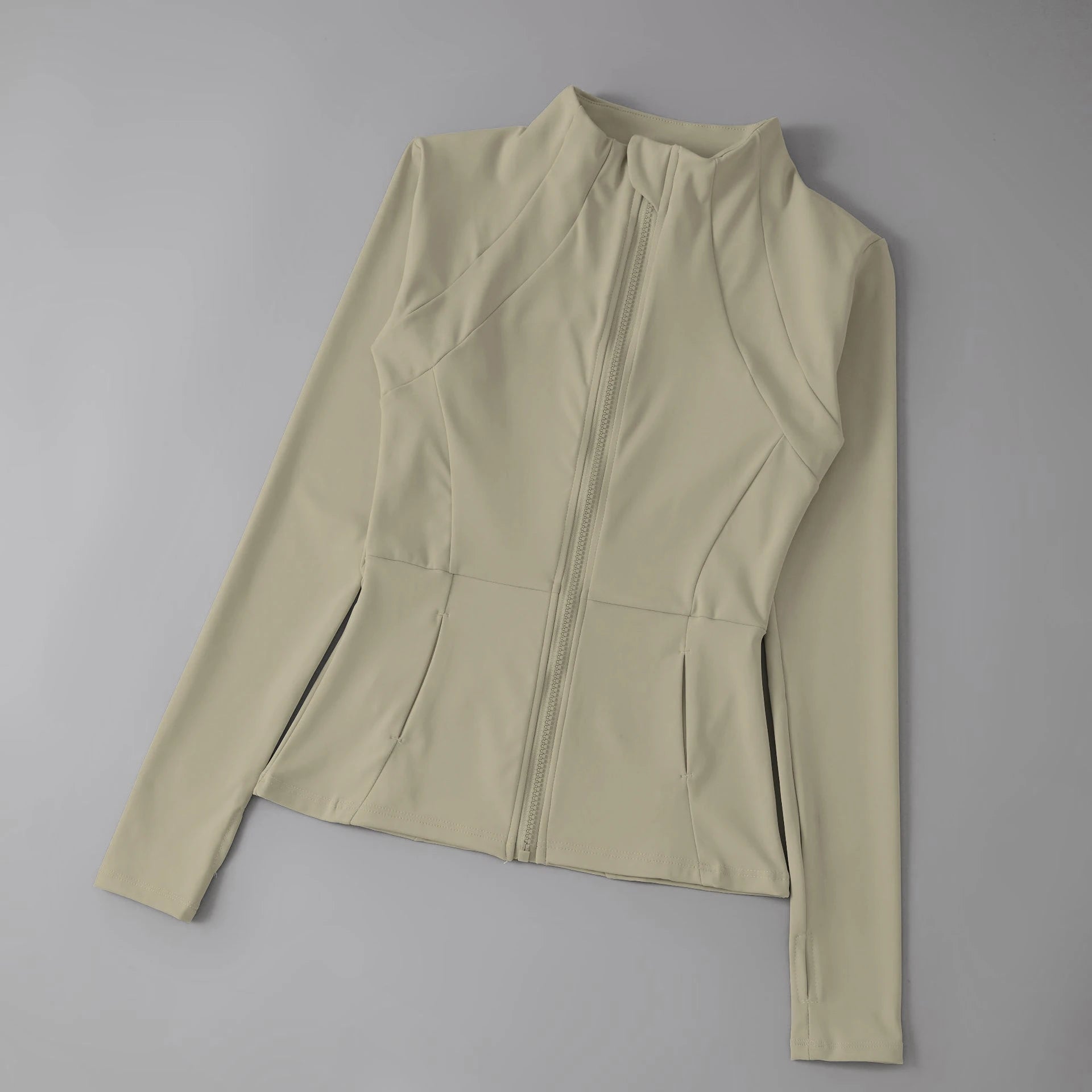 Beige long-sleeved athletic zip-up jacket with a high neck, fitted silhouette, and thumbhole cuffs.