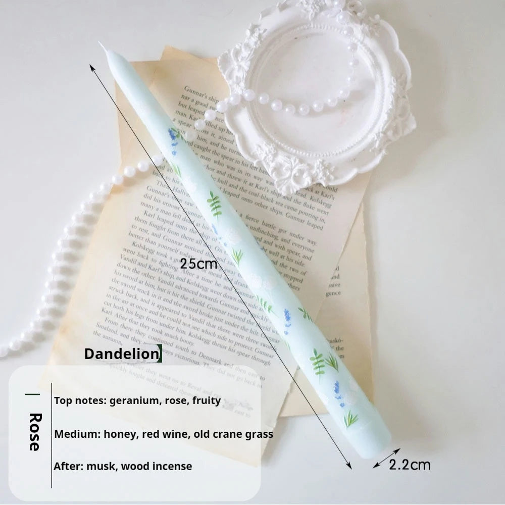 Pale blue 25cm taper candle featuring a delicate green and blue dandelion print, laid on vintage paper.