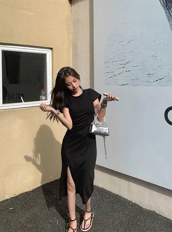 A woman wearing a black short-sleeved midi dress with a side slit, styled with a silver metallic handbag.