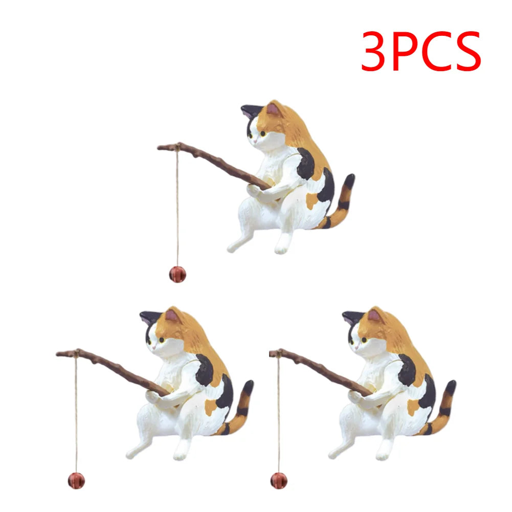 A set of three miniature calico cat ornaments, each sitting and holding a small fishing rod with a dangling bead.