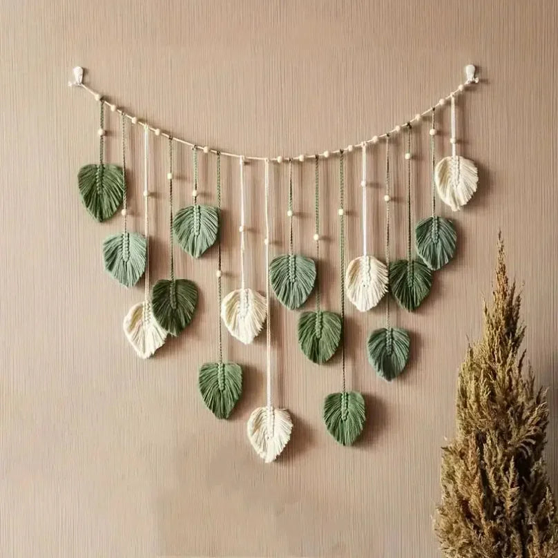 Macrame wall hanging featuring sage green and cream leaf-shaped tassels suspended from a bead-accented string.