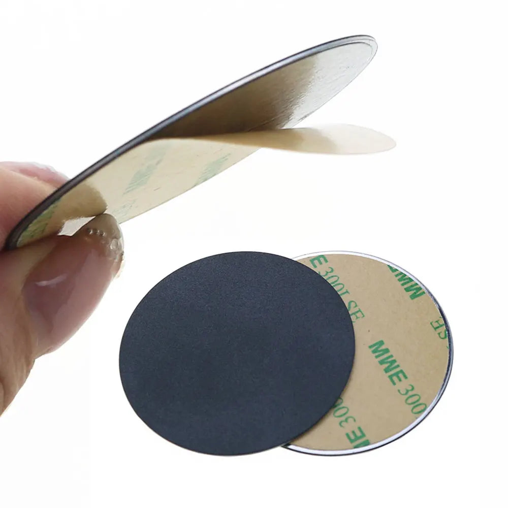 Hand holding round, black adhesive circular stickers with protective tan backing paper being peeled off.