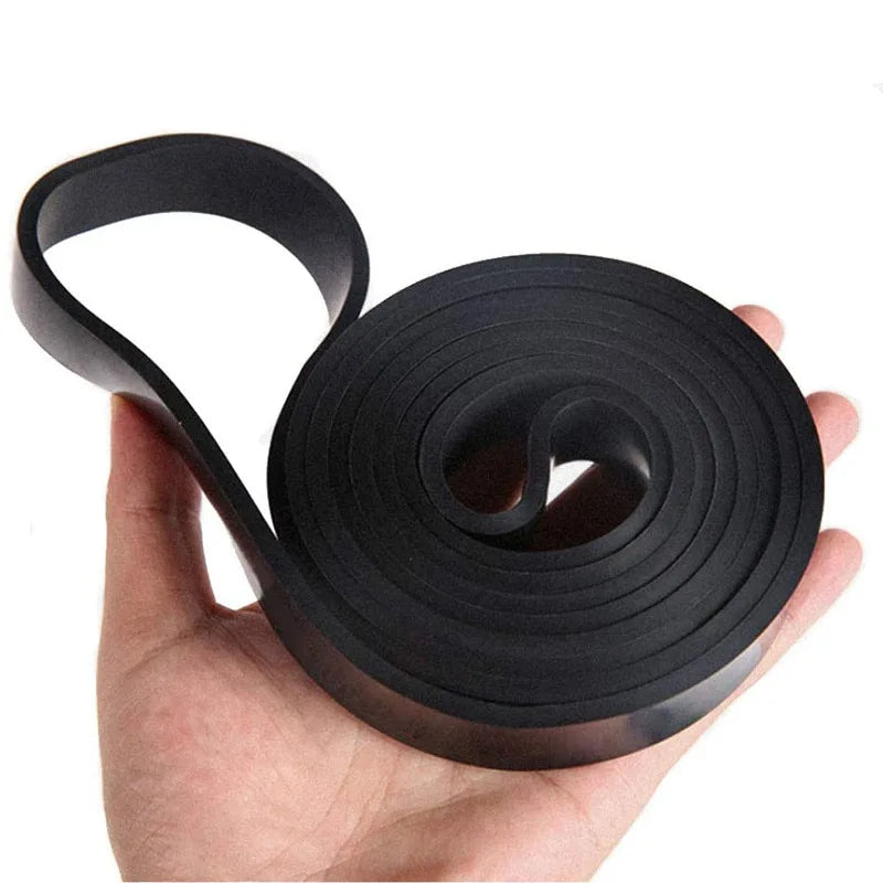 A coiled black rubber resistance band for gym training held in the palm of a hand.