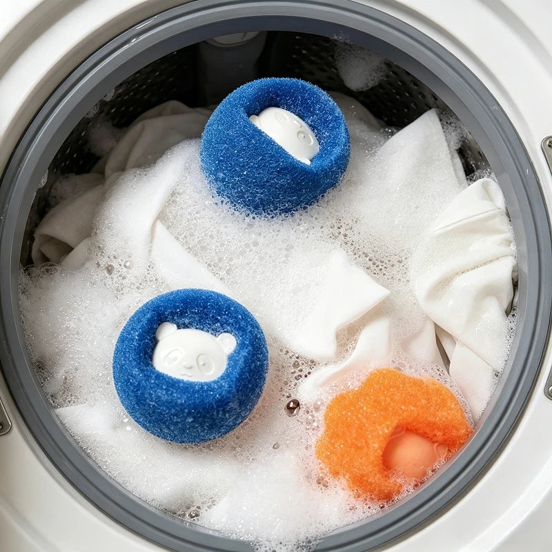 Two blue and one orange sponge laundry balls with cute animal faces in a washing machine with suds and white clothes.