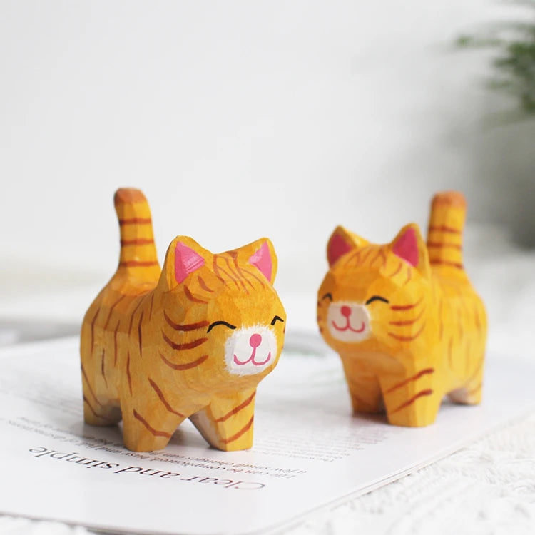 Two small, hand-carved orange tabby cat wooden figurines with happy expressions and upright tails.