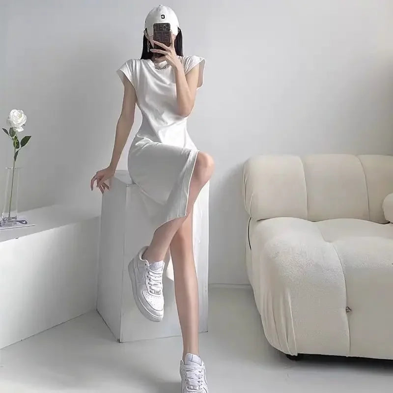 Woman wearing a white, cap-sleeve midi t-shirt dress with a side slit, paired with white trainers.