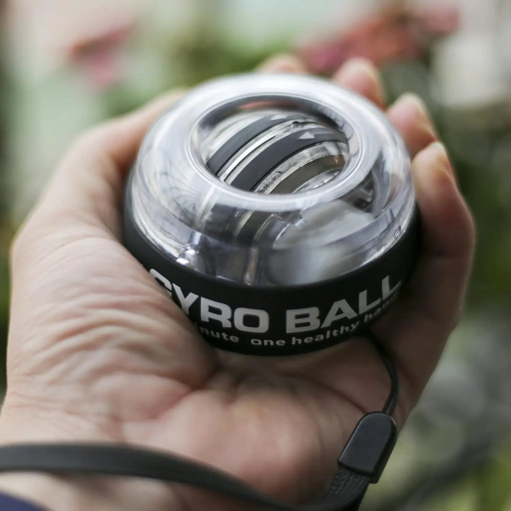 A hand holding a black and clear plastic gyro exercise ball with a black wrist strap.